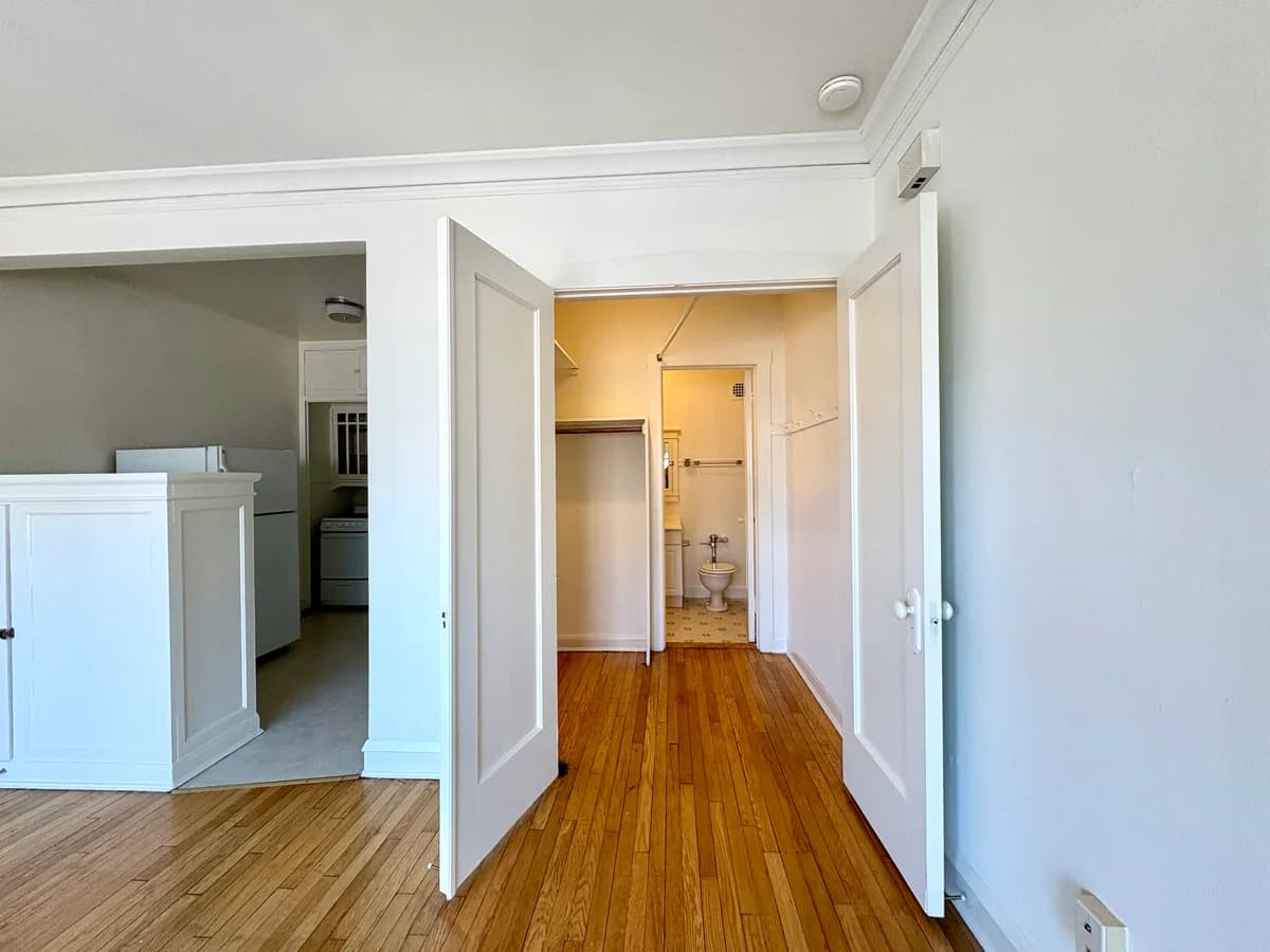 Milwaukee County apartments for rent - image - Inviting apartment interior showcasing a bright hallway with wooden flooring, leading to a kitchen and bathroom, featuring elegant white doors.