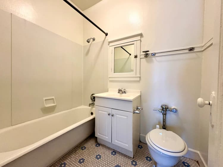 Milwaukee County apartments for rent - image - Bright bathroom with classic white fixtures, featuring a bathtub, elegant hexagonal tile flooring, and a stylish vanity with a mirrored cabinet.