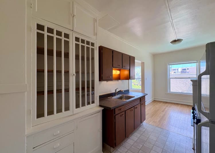 Milwaukee County apartments for rent - image - Bright and inviting kitchen with sleek wooden cabinets, a large window for natural light, and classic built-in shelving, offering a perfect blend of style and functionality.