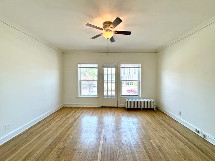 Milwaukee County apartments for rent - image - Bright and spacious living room with polished hardwood floors, large windows, and a ceiling fan, offering cozy urban views.