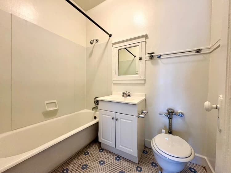 Milwaukee County apartments for rent - image - Bright bathroom with classic white fixtures, featuring a bathtub, elegant hexagonal tile flooring, and a stylish vanity with a mirrored cabinet.