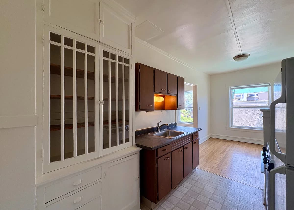 Milwaukee County apartments for rent - image - Bright and inviting kitchen with sleek wooden cabinets, a large window for natural light, and classic built-in shelving, offering a perfect blend of style and functionality.